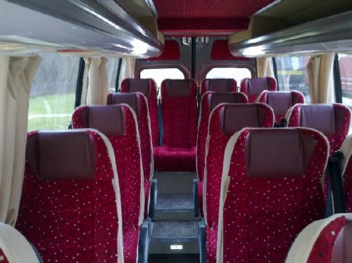 Czerwone fotele pasażerów w busie. Oferta wynajmu transportu.