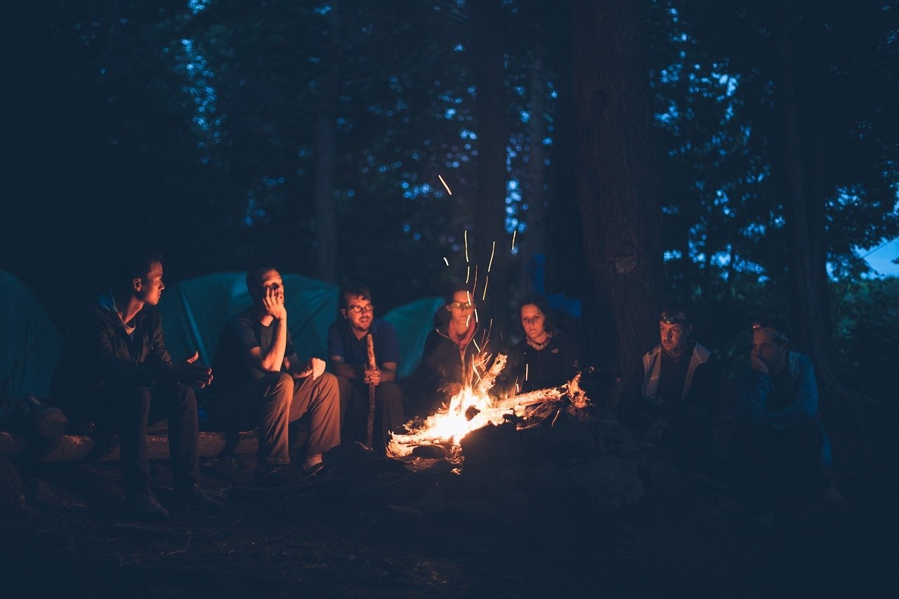 grupka ludzi siedzących nocą przy ognisku